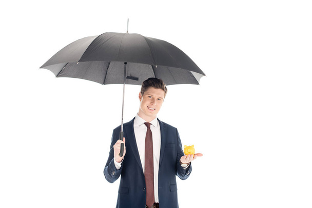 sonriente hombre de negocios con paraguas sosteniendo pequeña alcancía aislada en blanco
 - Foto, Imagen