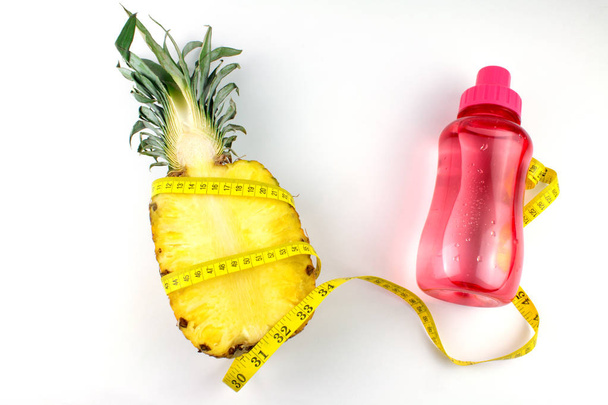 polovina žlutého čerstvého ananasu, měřicí páska a růžová sportovní láhev s vodou izolovanou na bílém  - Fotografie, Obrázek