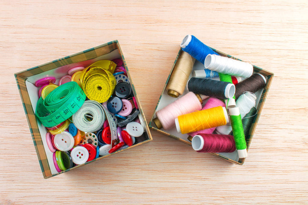 Colorful threads and measuring tapes in box on wooden background - Photo, Image