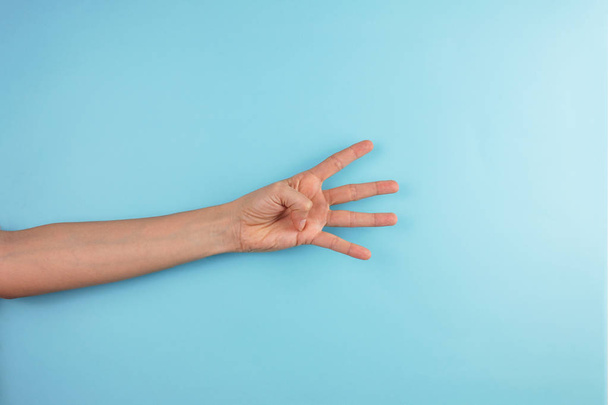 обрізаний знімок жіночої руки, що показує чотири пальці на синьому фоні
 - Фото, зображення