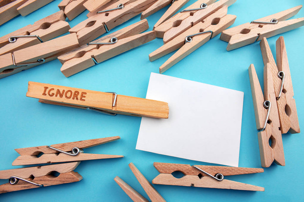 wooden clothespins with ignore sign and empty card on blue background - Photo, Image