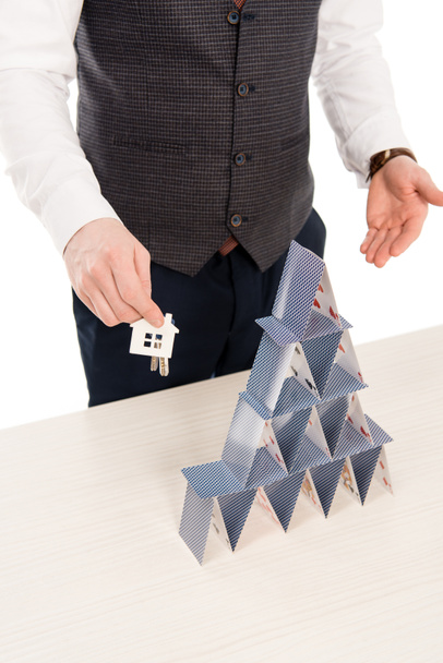 cropped view of real estate agent holding house keys and showing pyramid from playing cards, isolated on white - Photo, Image