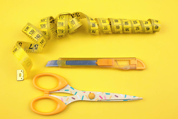 Coupe en plastique jaune, ciseaux et ruban à mesurer sur fond de papier
 - Photo, image