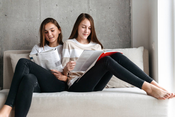 Two smiling teenage girls reading magazines - Fotó, kép