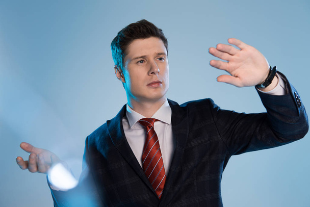 selective focus of young businessman in suit gesturing on blue - Фото, зображення