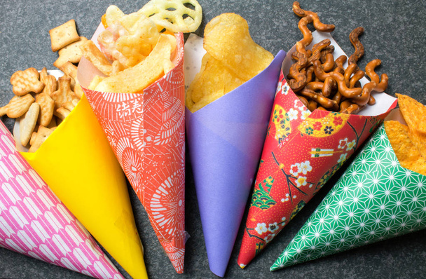 Muchos tipos de snacks en conos de papel sobre mesa rústica oscura
 - Foto, imagen