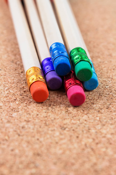 lápis de madeira com borrachas coloridas sobre fundo de cortiça
 - Foto, Imagem