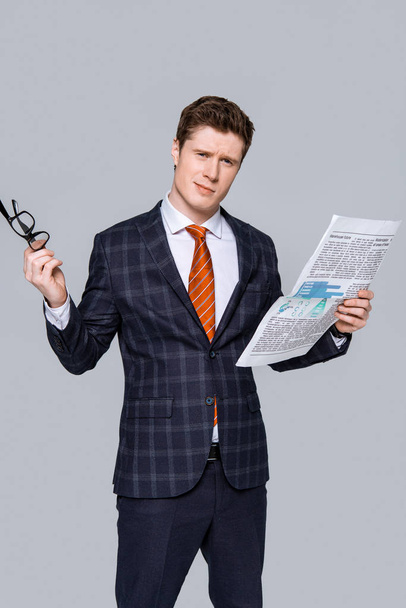 young businessman holding glasses and newspaper isolated on grey - Фото, изображение