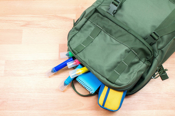 close-up shot of backpack with colorful markers and art supplies on wooden surface - Fotó, kép