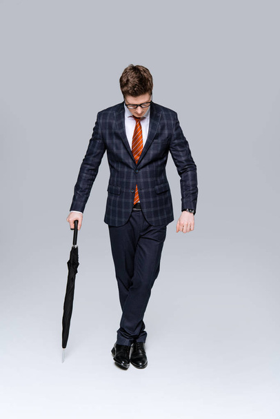 stylish businessman in suit posing with umbrella isolated on grey - Zdjęcie, obraz