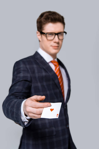 Selektive Fokussierung des stilvollen Geschäftsmannes, der sein Ass isoliert auf Grau hält  - Foto, Bild