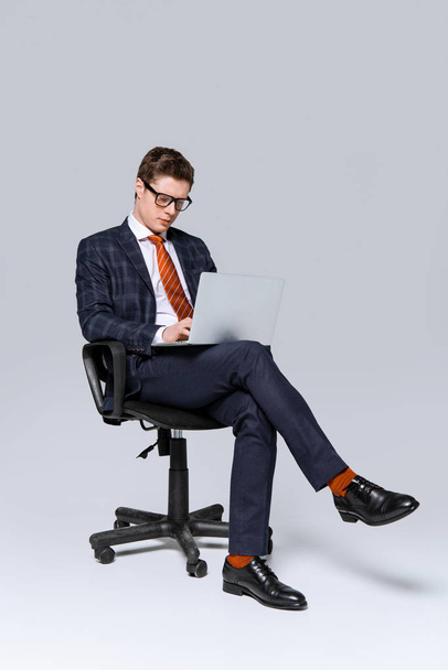 businessman sitting on chair and working on laptop on grey - Фото, зображення