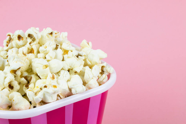 Popcorn in roze gestreepte emmer op roze achtergrond - Foto, afbeelding