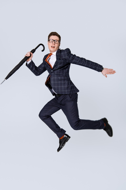 stylish young businessman jumping with umbrella isolated on grey - Photo, Image