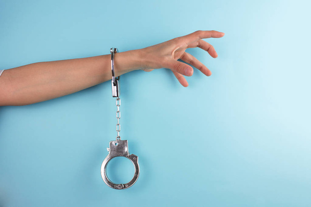 обрезанный снимок женской руки с наручниками на синем фоне
 - Фото, изображение