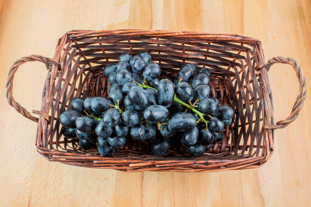 Ramo de uvas azules en canasta de mimbre sobre mesa de madera
 - Foto, imagen