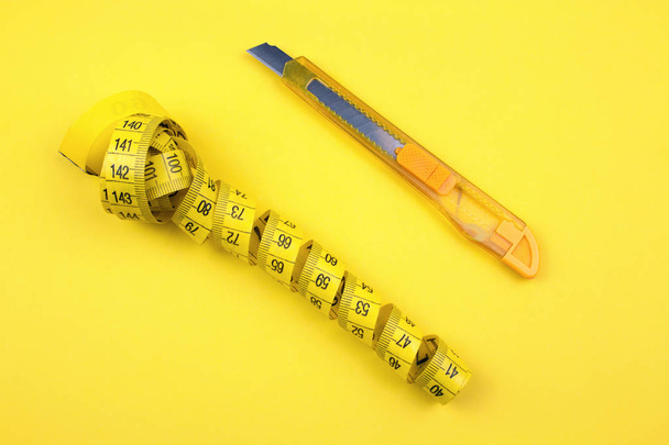Gelber Kunststoffschneider und Maßband auf Papierhintergrund - Foto, Bild