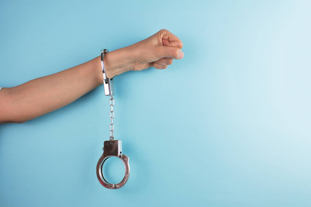 cropped shot of female hand with handcuff on blue background - Photo, Image