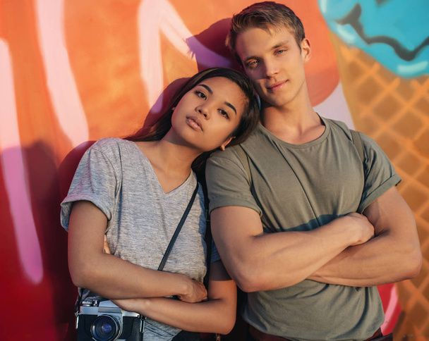 Portrait of a young couple with attitude standing side by side with their arms crossed in front of a wall of graffiti in the city - Photo, image
