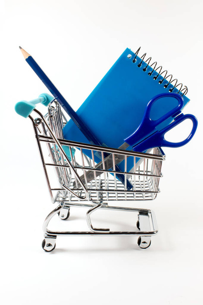 primer plano de la cesta de la compra con cuaderno, tijeras y lápiz en la superficie blanca
 - Foto, Imagen
