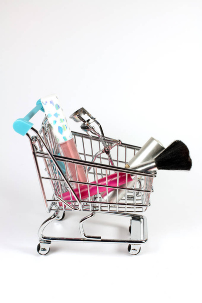 Nástroje pro kosmetiku a make-up v malém nákupním vozíku na bílém pozadí - Fotografie, Obrázek