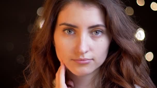 Close-up portret van de jonge Kaukasische meisje met golvende haar serieus kijken naar de camera op de achtergrond wazig lights. - Video