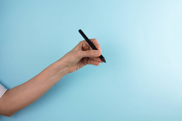 κομμένο πλάνο του γυναικείου χεριού που κρατά το στυλό σε μπλε φόντο - Φωτογραφία, εικόνα