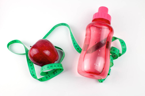 kırmızı elma, ölçüm bandı ve beyaz izole su pembe spor şişe  - Fotoğraf, Görsel