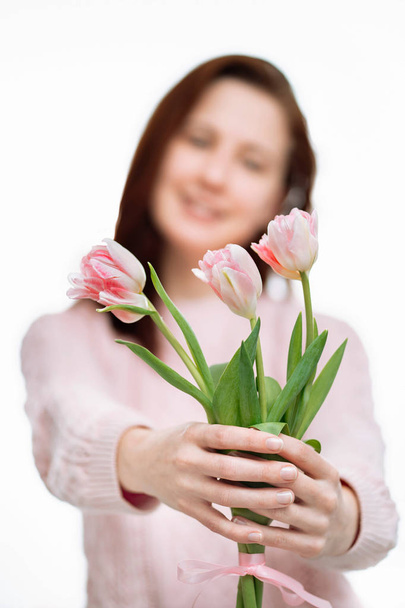 Young beautiful woman gives pink tulips on white background. - Foto, afbeelding