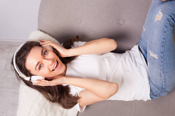 beautiful happy young woman lying on a sofa and enjoying music - Foto, Imagen