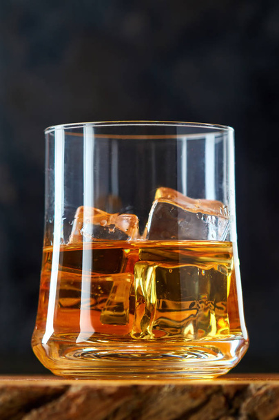 Glass of whiskey with ice cubes (on the rocks) on black background. Copy space - Zdjęcie, obraz