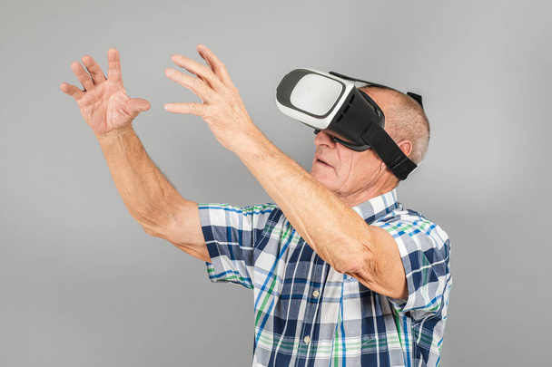 Grandfather looks into VR glasses, hand gestures, on a gray back - Fotó, kép