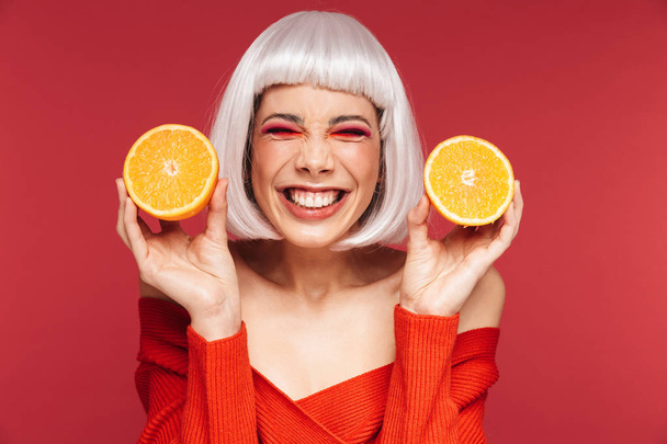 Beautiful young woman isolated over red wall background holding orange. - 写真・画像