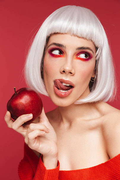 Beautiful young woman isolated over red wall background holding apple. - Fotografie, Obrázek