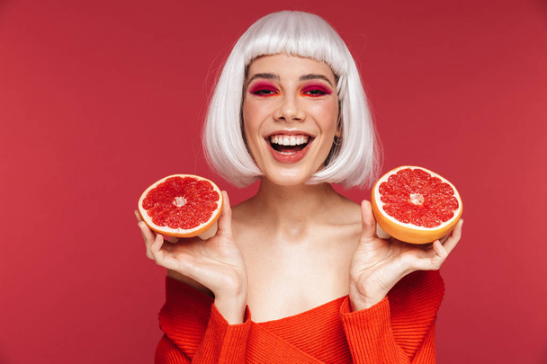 Cheerful beautiful young woman isolated over red wall background holding grapefruit. - Fotografie, Obrázek