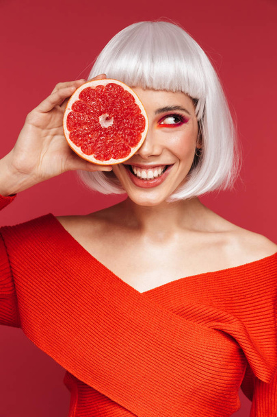 Cheerful beautiful young woman isolated over red wall background holding grapefruit. - Foto, imagen