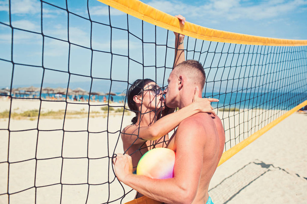 Love and flirting of couple. love relations of kissing couple at beach volleyball net holding ball. - Фото, изображение