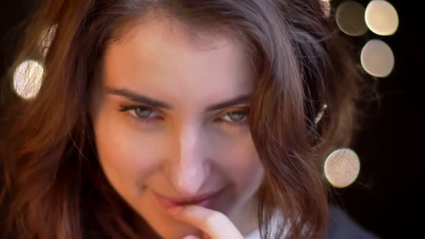 Close-up ritratto di giovane ragazza caucasica guardando umilmente in macchina fotografica su sfondo luci sfocate
. - Filmati, video