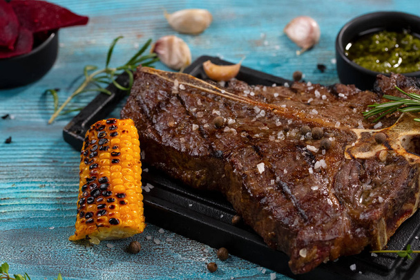 Közepes az ritka sült Steak Ribeye Fekete Angus a kukorica és a rozmaring, a szolgáló tábla blokk kék fa háttér - Fotó, kép