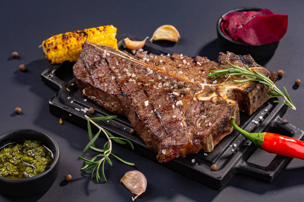 Medium rare grilled Steak Ribeye Black Angus with corn and rosemary on serving board block on black background - Photo, Image