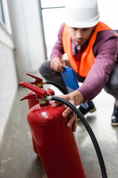 selective focus of red extinguishers near fireman with clipboard in hand - Фото, изображение