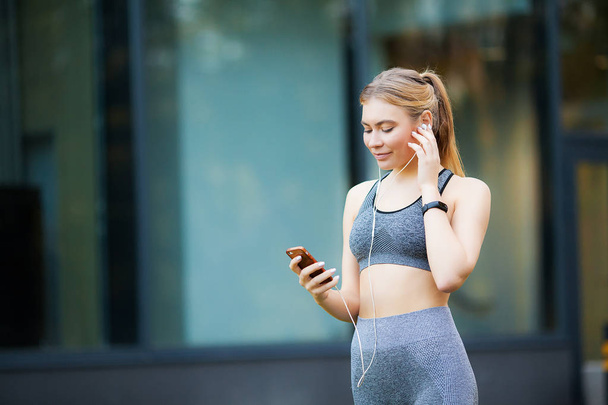 Fitness woman. Young sporty woman listens to music via a smartphone and earbuds - Photo, Image