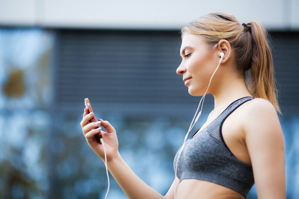 Fitness woman. Young sporty woman listens to music via a smartphone and earbuds - 写真・画像