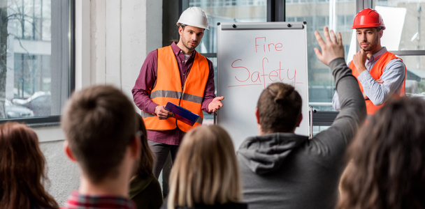 selective focus of handsome firemen in helmets giving talk on briefing near white board with fire safety lettering  - Foto, imagen