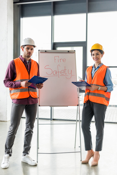 selective focus of fireman standing near attractive coworker near white board with fire safety lettering  - Photo, Image