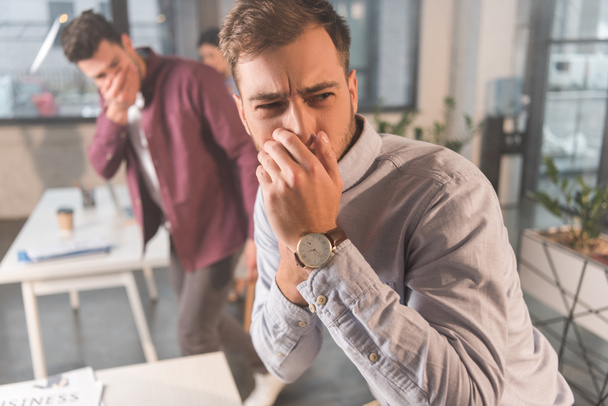handsome man holding nose near coworkers in office with smoke - Foto, Imagem