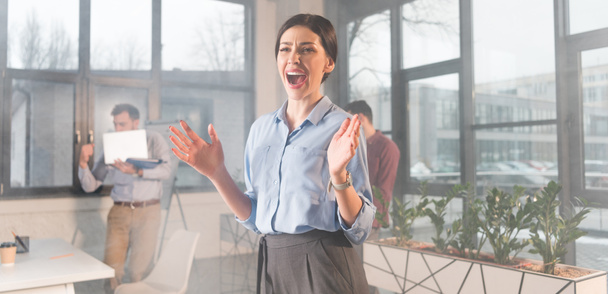 scared businesswoman screaming while standing near coworkers in office with smoke - Foto, imagen