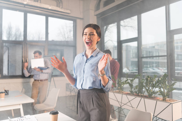 attractive businesswoman standing and screaming near coworkers in office with smoke - Valokuva, kuva