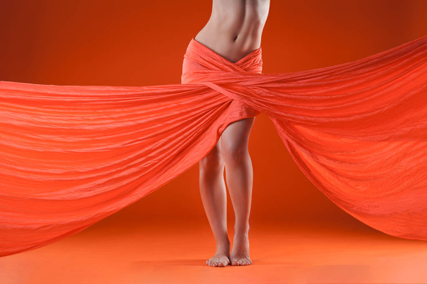 beautiful female body with fabric loop on a orange background - Foto, afbeelding
