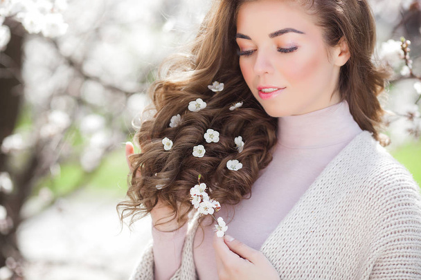 Vonzó fiatal nő göndör hajú kültéri. Gyönyörű hölgy Vértes portré a tavaszi háttér. Nő, fehér virágok a haját. Modellalkotó modell. - Fotó, kép